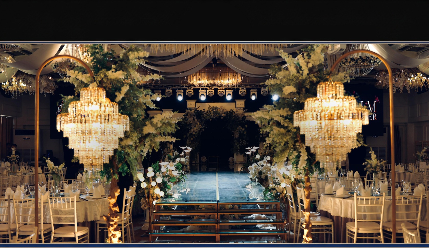 Candlelit wedding reception with crystal chandeliers, white floral arches and a mirrored runway